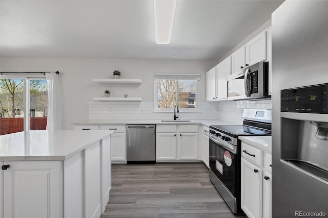 kitchen featuring light countertops, stainless steel appliances, open shelves, and a sink