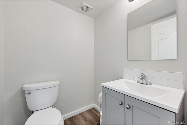 half bathroom with visible vents, vanity, wood finished floors, toilet, and baseboards