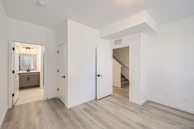 unfurnished bedroom with sink, light hardwood / wood-style floors, and ensuite bath