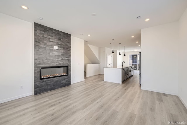 unfurnished living room featuring sink, a large fireplace, and light hardwood / wood-style floors