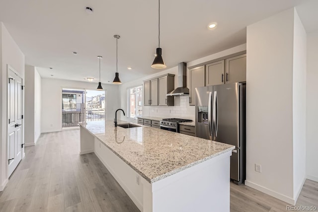 kitchen with wall chimney exhaust hood, stainless steel appliances, sink, and a center island with sink