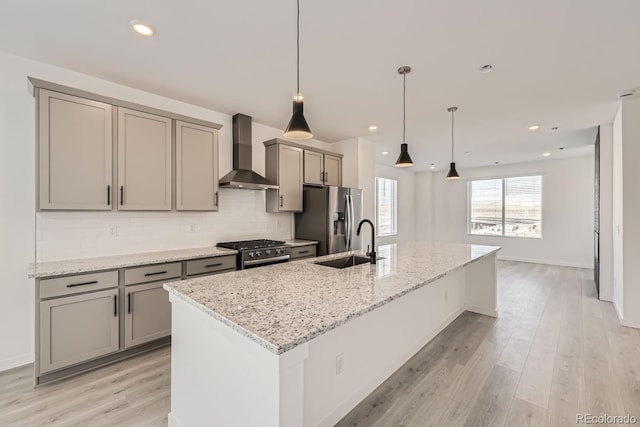 kitchen with stainless steel appliances, an island with sink, light stone counters, and wall chimney exhaust hood