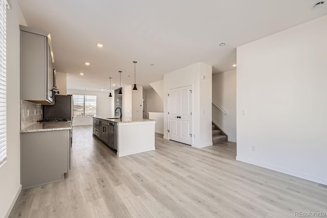 kitchen with sink, light hardwood / wood-style flooring, gray cabinets, hanging light fixtures, and a center island with sink