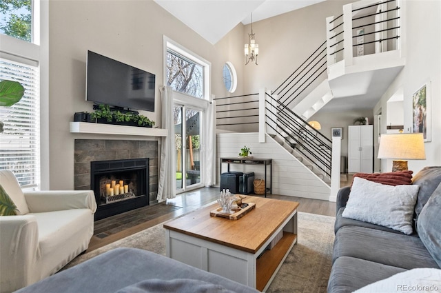 living room featuring a tiled fireplace, dark wood-type flooring, a healthy amount of sunlight, and a towering ceiling