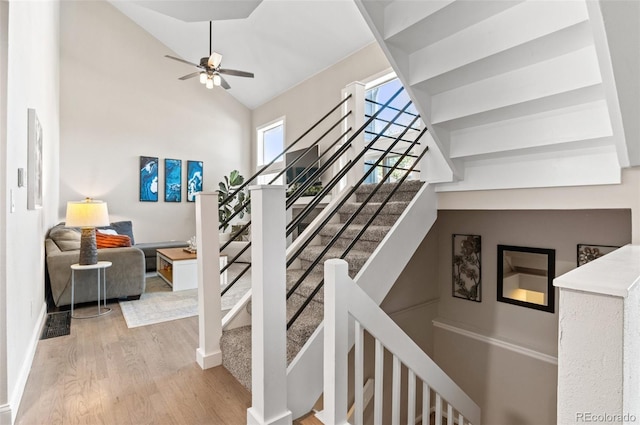 staircase with high vaulted ceiling, ceiling fan, and light wood-type flooring