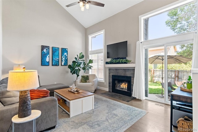 living room with a tile fireplace, high vaulted ceiling, wood-type flooring, and a healthy amount of sunlight