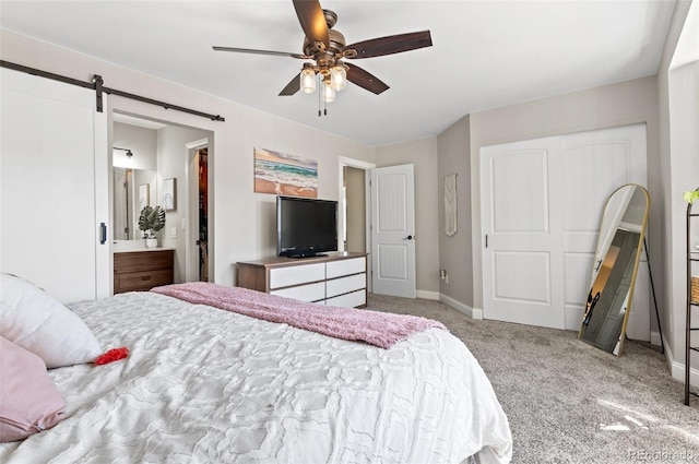 carpeted bedroom featuring ensuite bath, a barn door, and ceiling fan