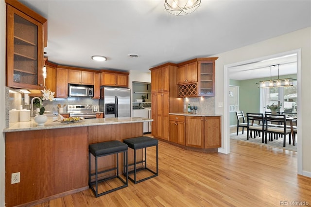 3190 Ward Ct, Wheat Ridge, CO 80215 - kitchen with stainless steel appliances, washing machine and clothes dryer, decorative backsplash, a peninsula, and light wood-type flooring