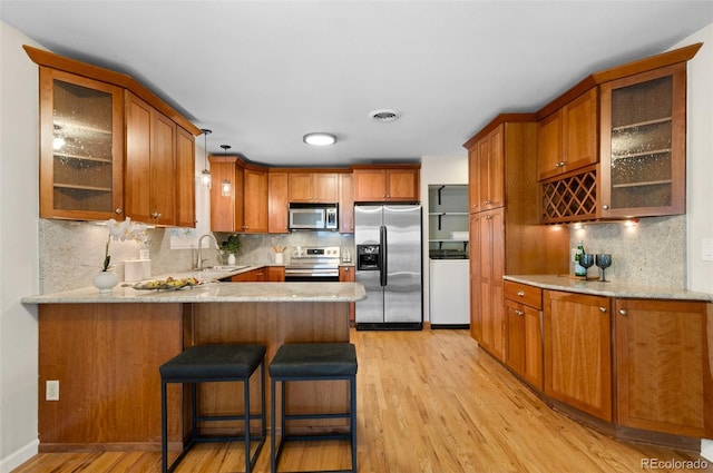 3190 Ward Ct, Wheat Ridge, CO 80215 - kitchen with stainless steel appliances, a sink, washer / dryer, brown cabinetry, and light wood-style flooring