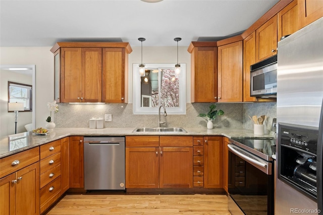 3190 Ward Ct, Wheat Ridge, CO 80215 - kitchen featuring stainless steel appliances, a sink, brown cabinetry, light wood-style floors, and light stone countertops