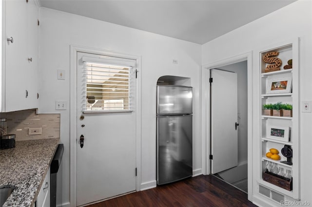 kitchen with dark wood-type flooring, light stone counters, stainless steel fridge, white cabinets, and backsplash