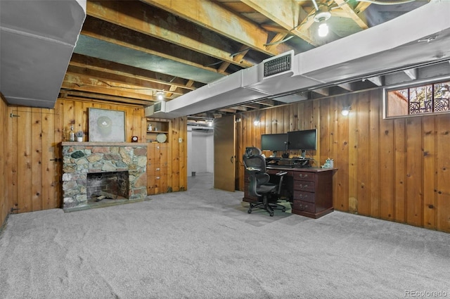 office with a stone fireplace, carpet floors, and wood walls