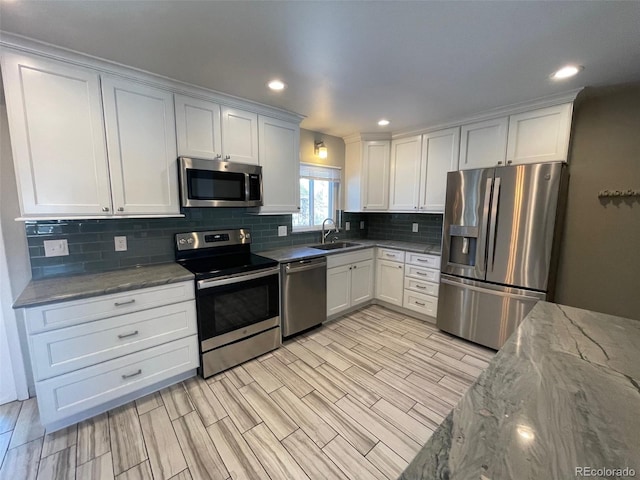 kitchen with white cabinetry, appliances with stainless steel finishes, sink, and light stone counters