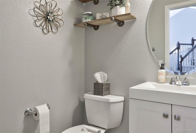 bathroom featuring toilet, vanity, and a textured wall