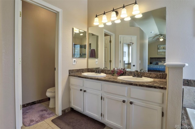 ensuite bathroom featuring ceiling fan, toilet, double vanity, tile patterned flooring, and a fireplace