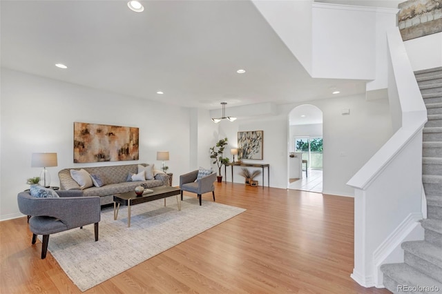 living area with recessed lighting, arched walkways, light wood-style flooring, and stairs