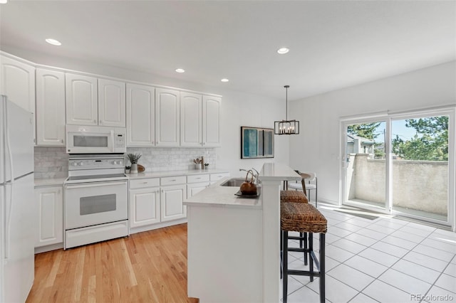 kitchen featuring decorative backsplash, white appliances, a breakfast bar area, and white cabinets