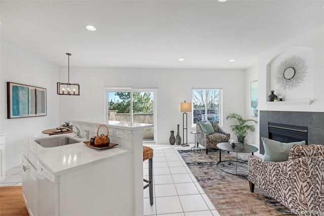 kitchen with an island with sink, a tiled fireplace, a sink, open floor plan, and light tile patterned flooring