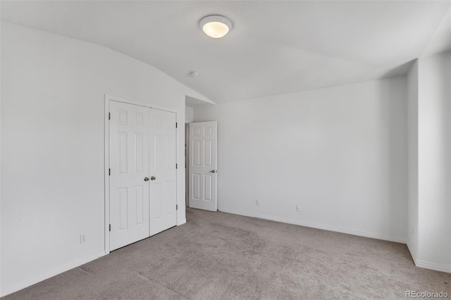 carpeted spare room featuring lofted ceiling and baseboards