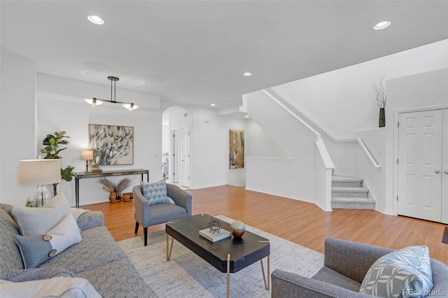 living area featuring arched walkways, stairway, recessed lighting, and light wood-style floors