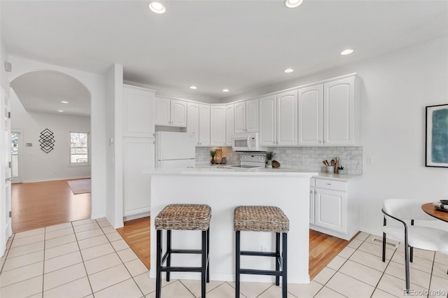 kitchen with light wood-style flooring, arched walkways, white cabinetry, white appliances, and a breakfast bar area