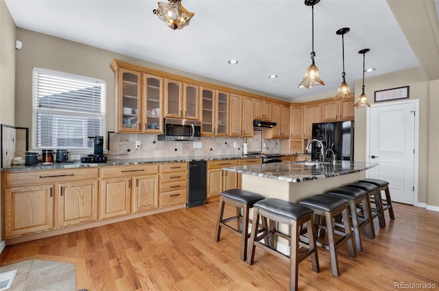 kitchen with stone counters, light hardwood / wood-style floors, a center island with sink, black refrigerator with ice dispenser, and a kitchen breakfast bar