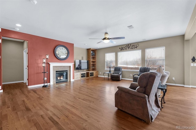 living room featuring ceiling fan, a tiled fireplace, and hardwood / wood-style flooring