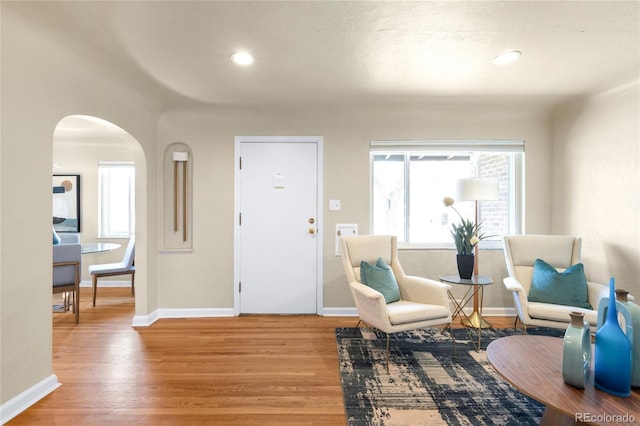 sitting room with a wealth of natural light, baseboards, arched walkways, and wood finished floors