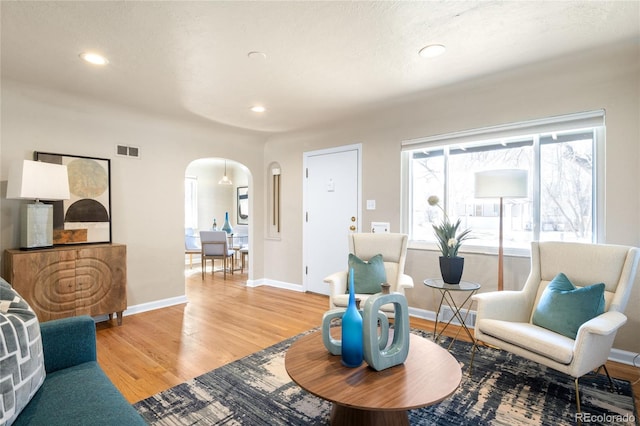 living area with visible vents, baseboards, light wood-style flooring, recessed lighting, and arched walkways