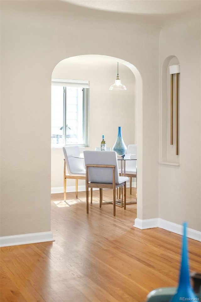 dining space featuring baseboards, arched walkways, and light wood-style flooring