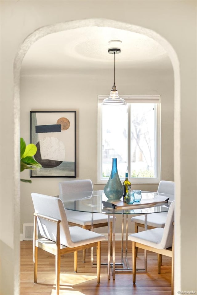 dining room with visible vents, wood finished floors, arched walkways, and baseboards