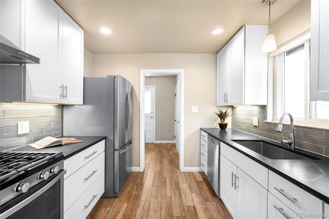 kitchen featuring dark countertops, stainless steel appliances, white cabinetry, wall chimney exhaust hood, and a sink