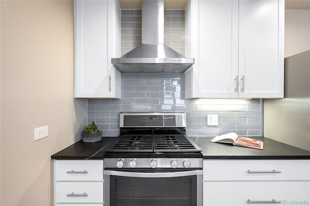 kitchen featuring stainless steel gas range, white cabinets, dark countertops, wall chimney exhaust hood, and backsplash