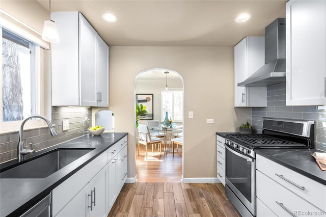 kitchen with dark countertops, stainless steel appliances, wall chimney exhaust hood, and a sink