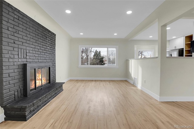 unfurnished living room featuring light hardwood / wood-style floors and a brick fireplace