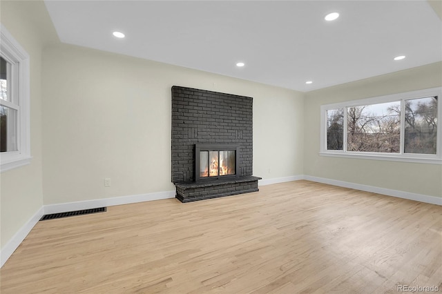 unfurnished living room featuring light hardwood / wood-style floors and a brick fireplace