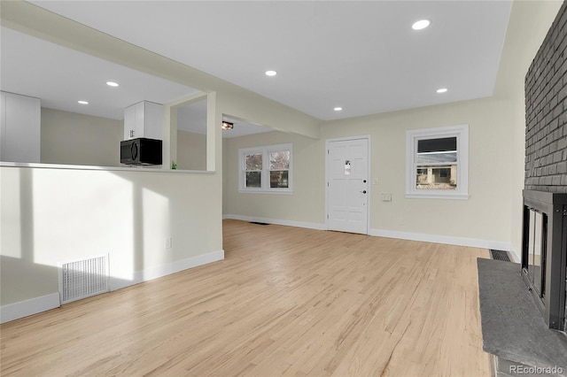 unfurnished living room featuring light wood-type flooring and a brick fireplace