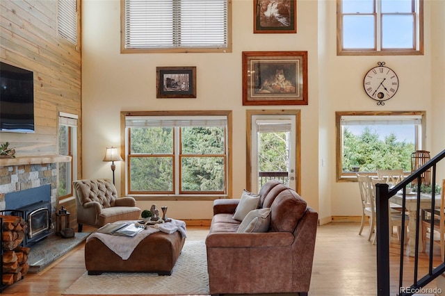 living room featuring light hardwood / wood-style flooring, wooden walls, a stone fireplace, and a towering ceiling