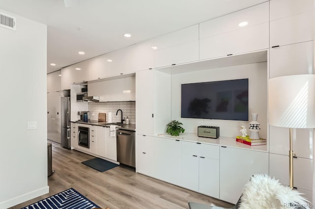 interior space with a sink, tasteful backsplash, appliances with stainless steel finishes, visible vents, and light wood-style floors