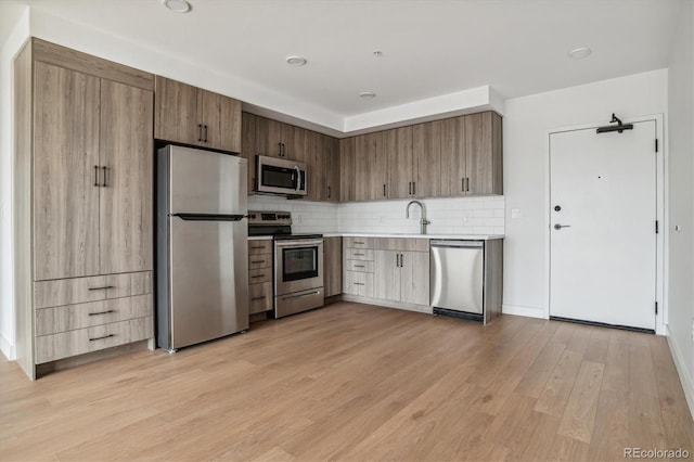 kitchen featuring light wood finished floors, a sink, backsplash, light countertops, and appliances with stainless steel finishes