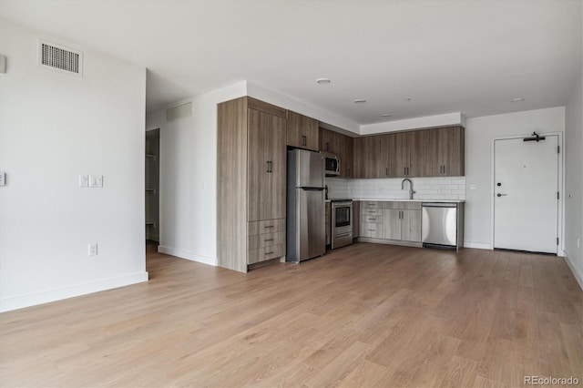 kitchen featuring stainless steel appliances, visible vents, a sink, decorative backsplash, and light countertops