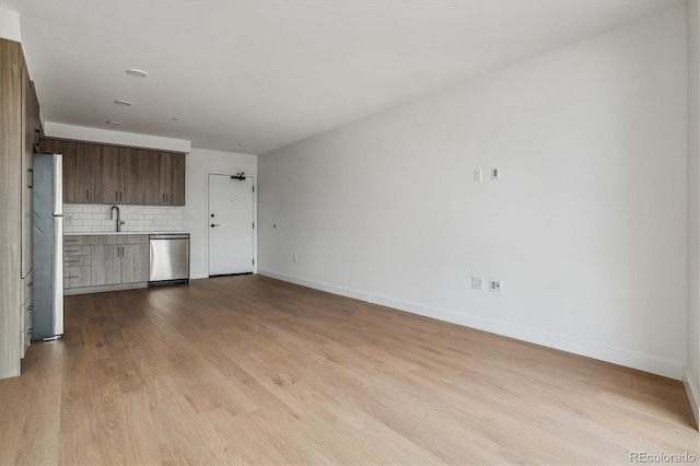unfurnished living room featuring baseboards, light wood finished floors, and a sink