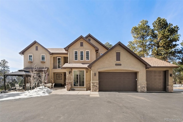 view of front facade featuring aphalt driveway, stone siding, stucco siding, and an attached garage