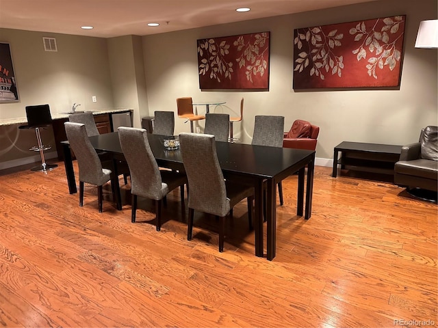 dining area featuring light wood finished floors, recessed lighting, bar, and baseboards
