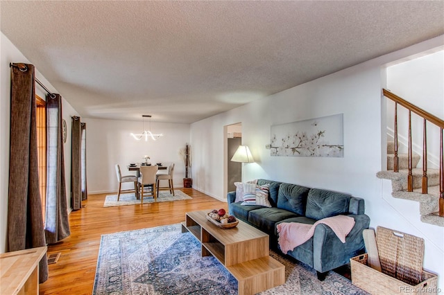 living area with baseboards, visible vents, light wood-style flooring, stairs, and a textured ceiling