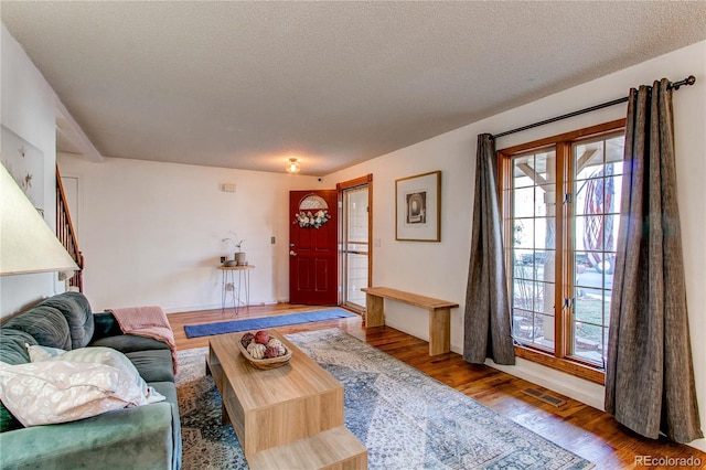 living room featuring visible vents, a textured ceiling, baseboards, and wood finished floors