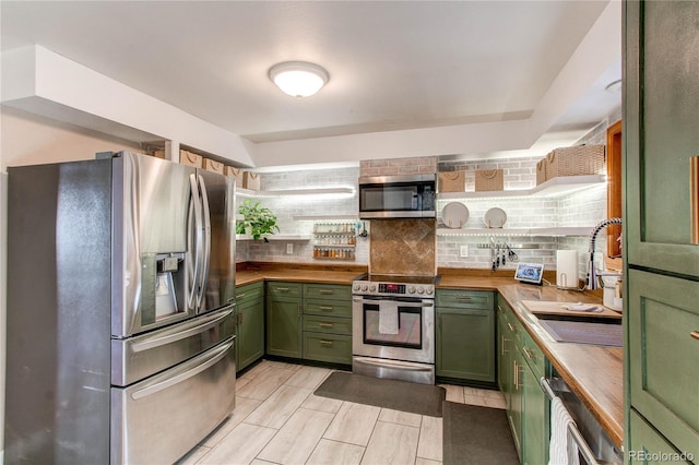 kitchen with tasteful backsplash, green cabinets, appliances with stainless steel finishes, a sink, and wood counters