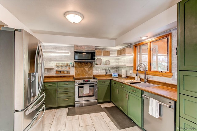 kitchen featuring wood counters, a sink, stainless steel appliances, green cabinets, and backsplash