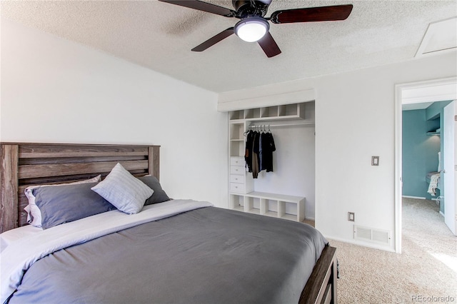 carpeted bedroom featuring a textured ceiling, a closet, visible vents, and a ceiling fan