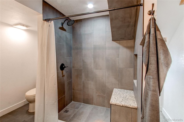 bathroom with toilet, baseboards, and tiled shower